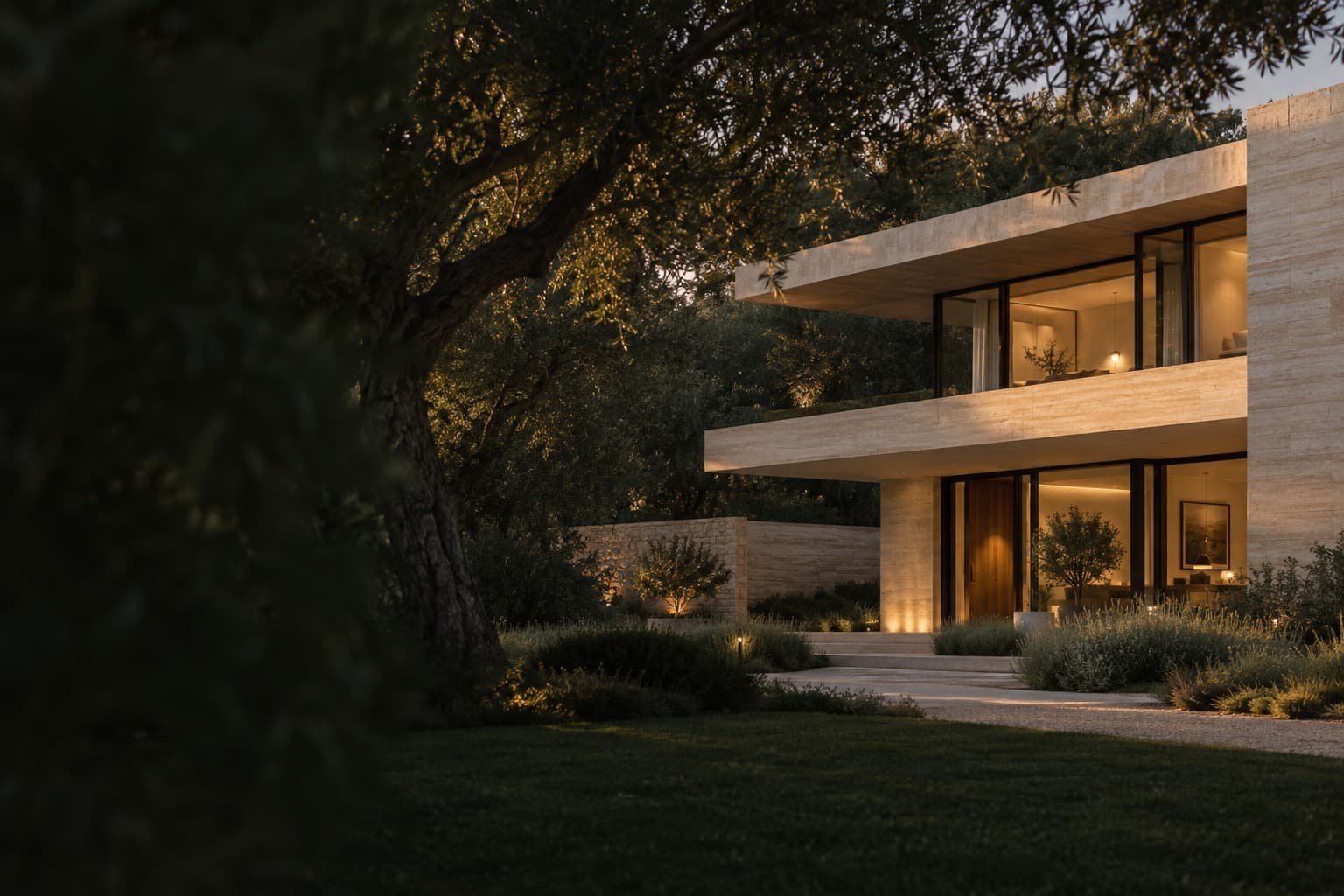 A warm stone home framed by an olive tree at dusk